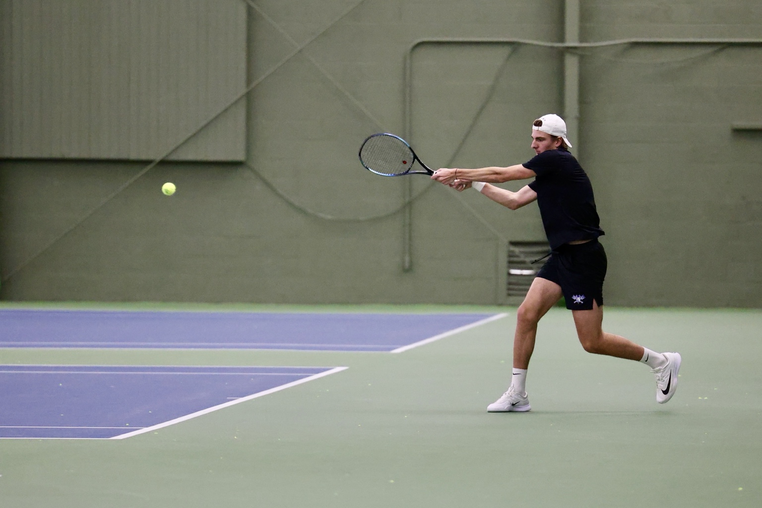 Augustin Patte playing a two-handed backhand on an indoor tennis court